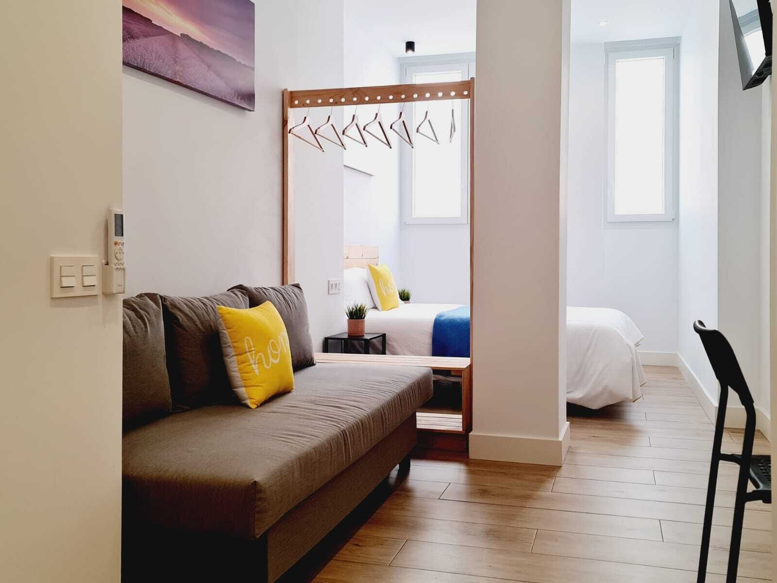 Un dormitorio moderno con sofá, cama, mesita de noche, espejo y ventana.