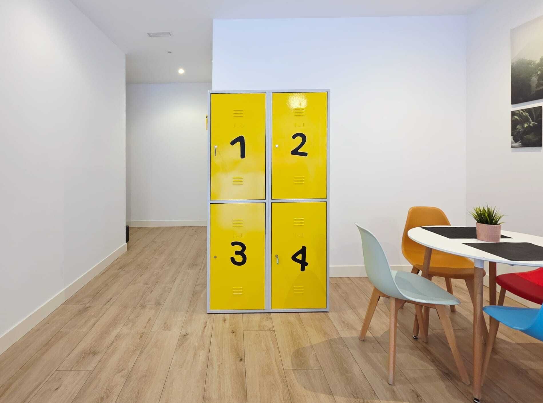 Un espacio de oficina moderno con suelo de madera, pared blanca y una mesa con sillas coloridas.