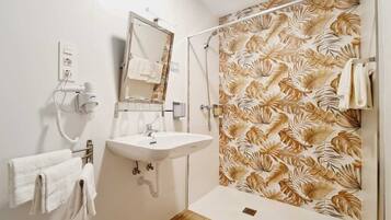 Een badkamer met een wastafel, spiegel, handdoekhouder en douche met een muur in bladerpatroon.