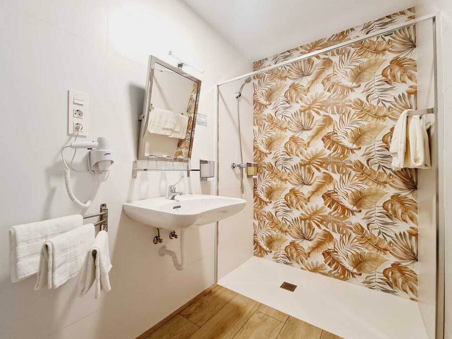 Een badkamer met een wastafel, spiegel, handdoekhouder en douche met een muur in bladerpatroon.