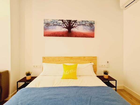 A bedroom with a bed, a nightstand, a wall-mounted picture, and a potted plant. - Bilbao ROOMS & KITCHEN Rekalde (Bilbao)