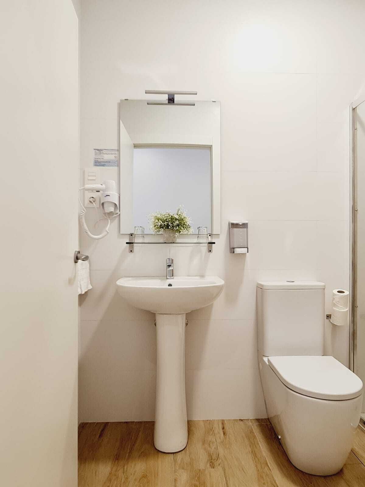 Un baño con lavamanos, espejo y retrete blancos.