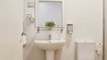 Un baño con lavamanos, espejo y retrete blancos.