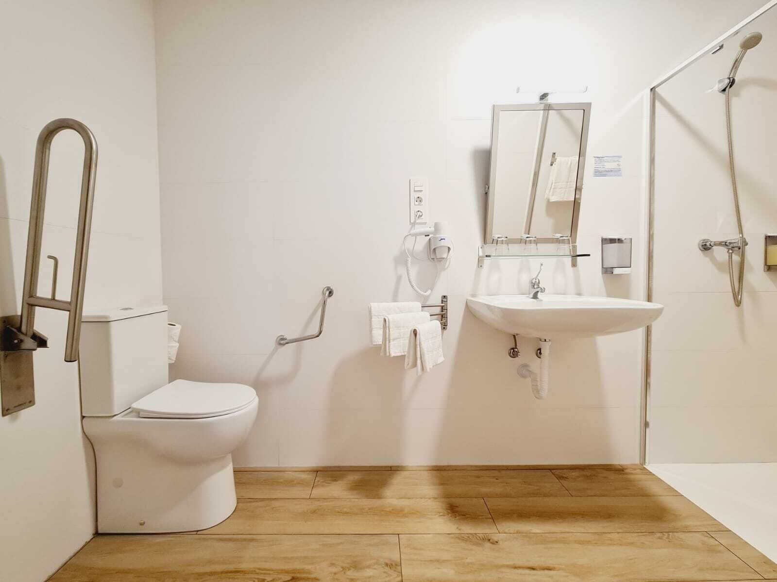 Un baño con inodoro, lavabo, ducha y barra de apoyo.