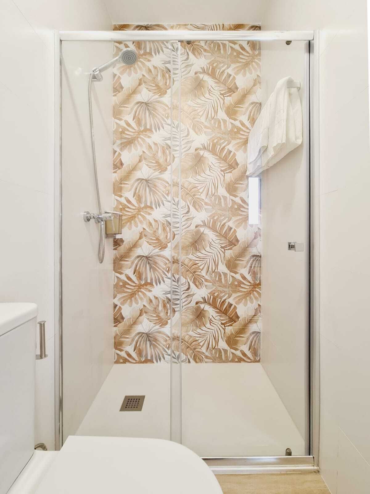 Ducha con motivos florales, una toalla blanca colgada en la pared y cabezal de ducha visible.