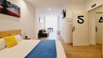 A hotel room with a bed, a sofa, a TV, and a hallway leading to a door marked with the number 5.