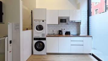 A compact kitchen with a washing machine, microwave, and a sink.
