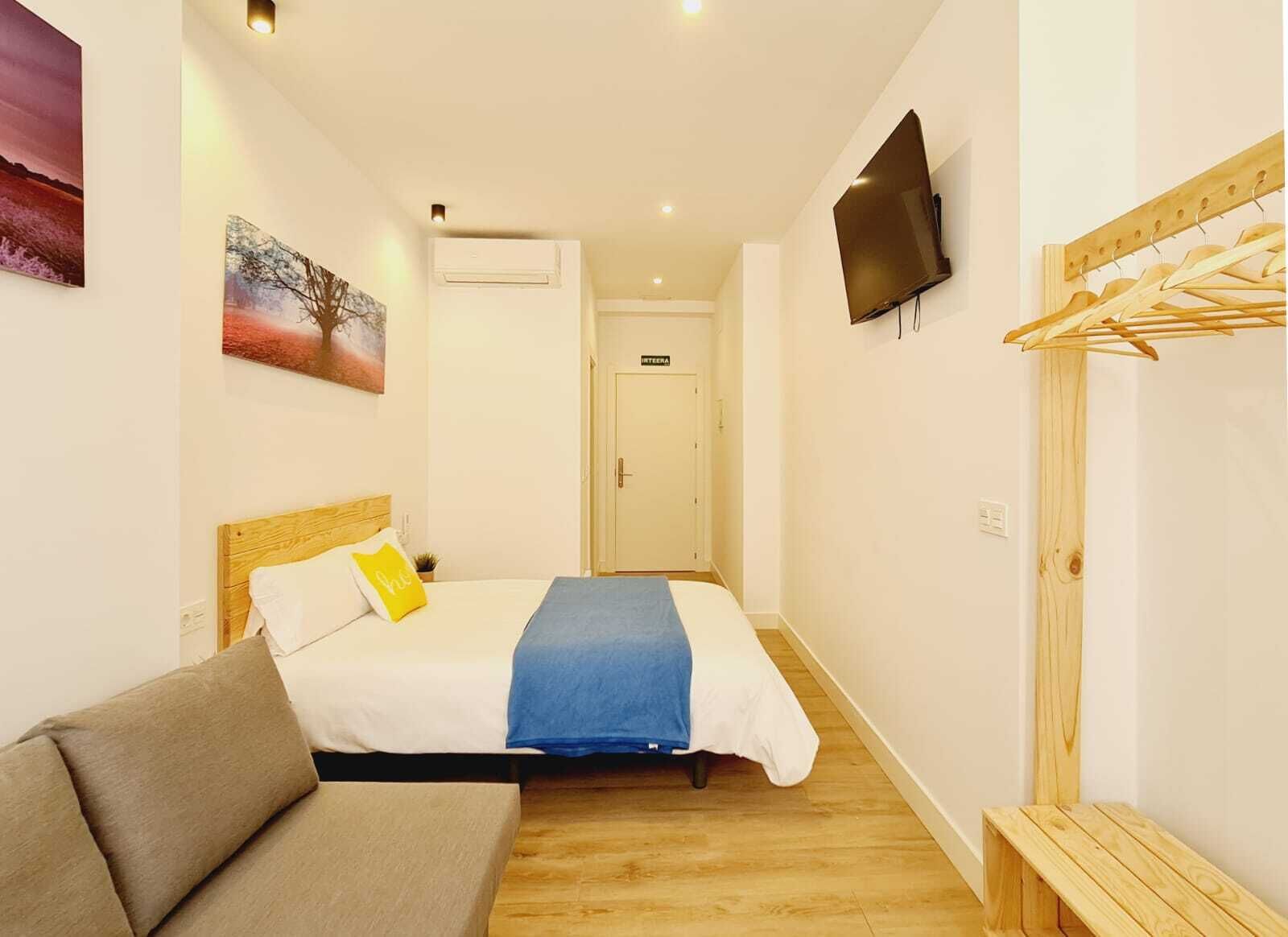 Un dormitorio con cama, televisor, banco de madera y perchero.