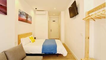 Un dormitorio con cama, televisor, banco de madera y perchero.