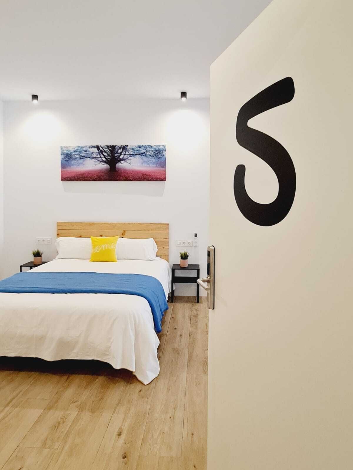 Quarto com cama, mesas de cabeceira, um criado-mudo, obra de arte na parede e um número grande na parede.