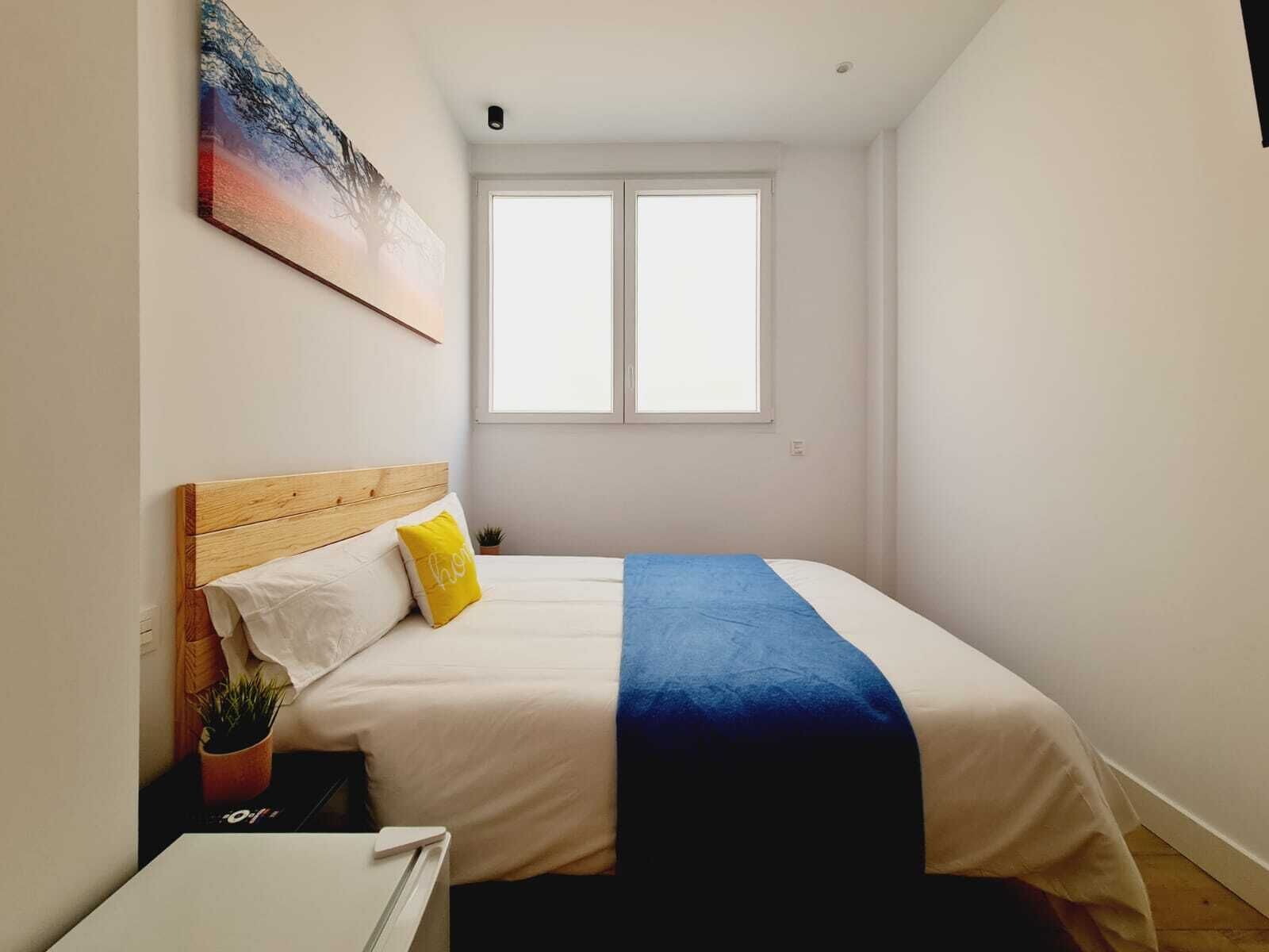 Una camera da letto con un letto, una finestra, un quadro e una piccola pianta.