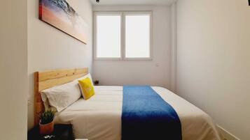 Una camera da letto con un letto, una finestra, un quadro e una piccola pianta.