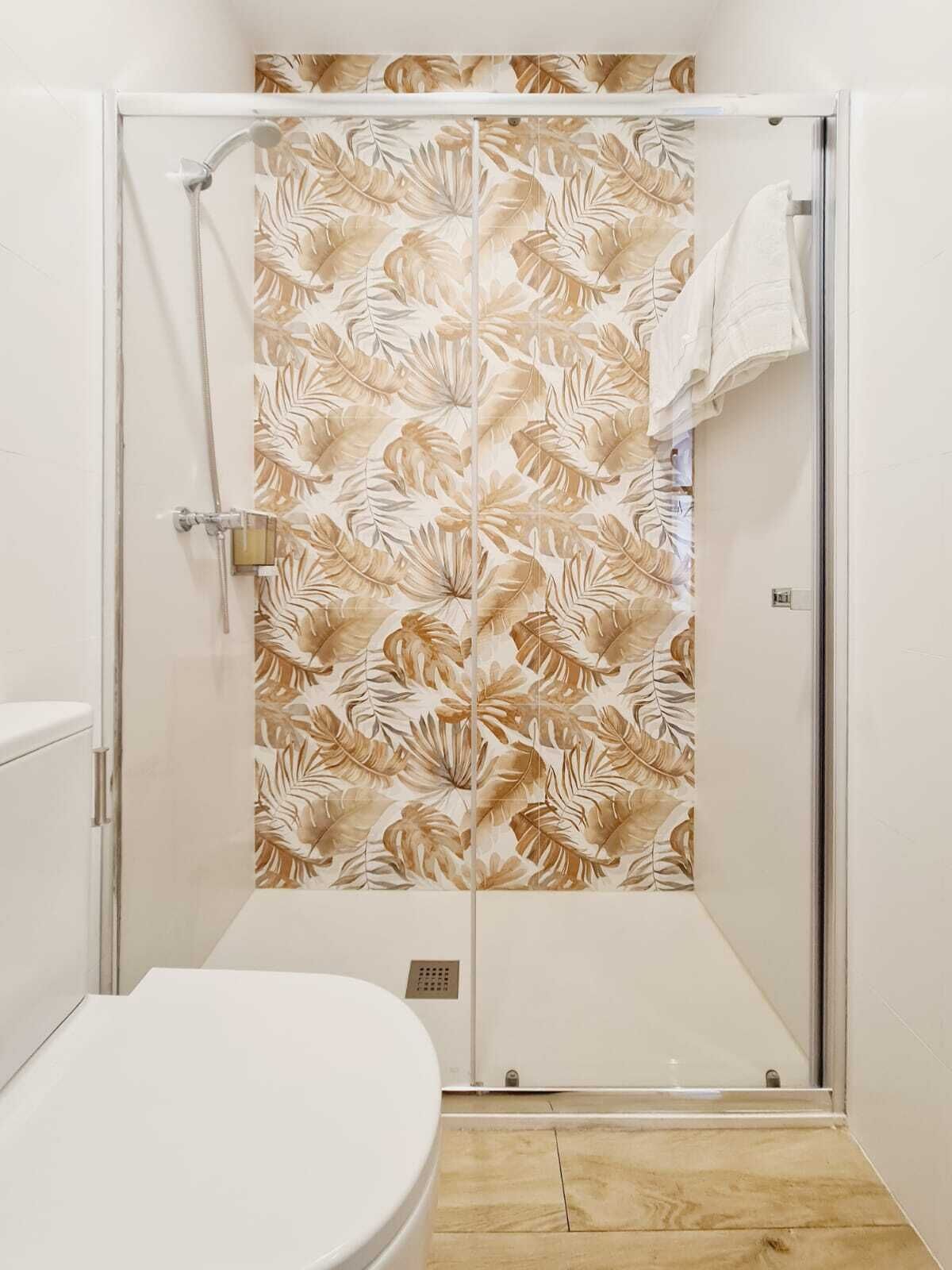 A shower with a leaf-patterned door, a white toilet, and a wooden floor.