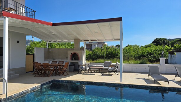 Ein Pool mit überdachter Terrasse, Sitzgelegenheiten im Freien und einem Backofen aus Ziegeln.
