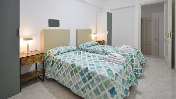 Ein Hotelzimmer mit zwei Betten, jeweils mit gemusterten Tagesdecken, Nachttischlampen und einem kleinen Tisch mit Lampe.