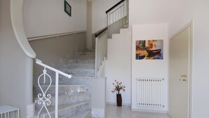 Eine Treppe mit Marmorstufen und einem weißen Geländer, die zu einer Zwischenebene mit einem Heizkörper und einem Gemälde führt.