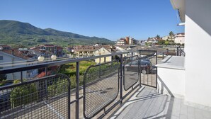 Ein Balkon mit Metallgeländer, der auf einen Wohnbereich mit Häusern und einem Berg im Hintergrund blickt.
