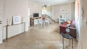 Un salon moderne avec un canapé, une table à manger et des chaises. Un escalier mène à un autre niveau.