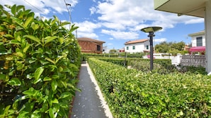 Un chemin bordé de haies soigneusement taillées, qui mène à un bâtiment surmonté d’un toit recouvert de tuiles rouges.