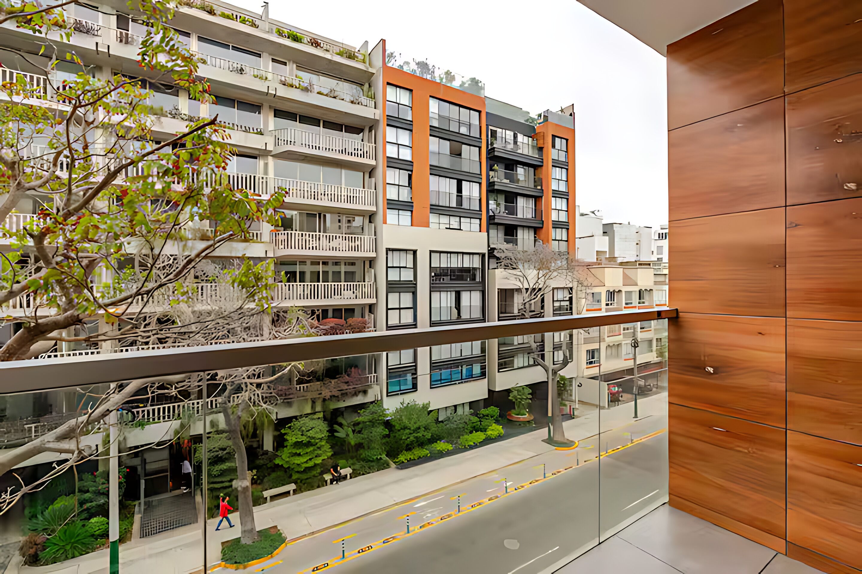 A modern apartment building with balconies, a glass railing, and a street view.