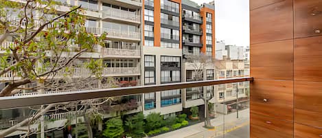 A modern apartment building with balconies, a glass railing, and a street view.