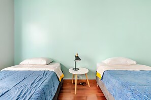 Ein Zimmer mit zwei Einzelbetten, einem kleinen runden Tisch mit Lampe und Holzboden.