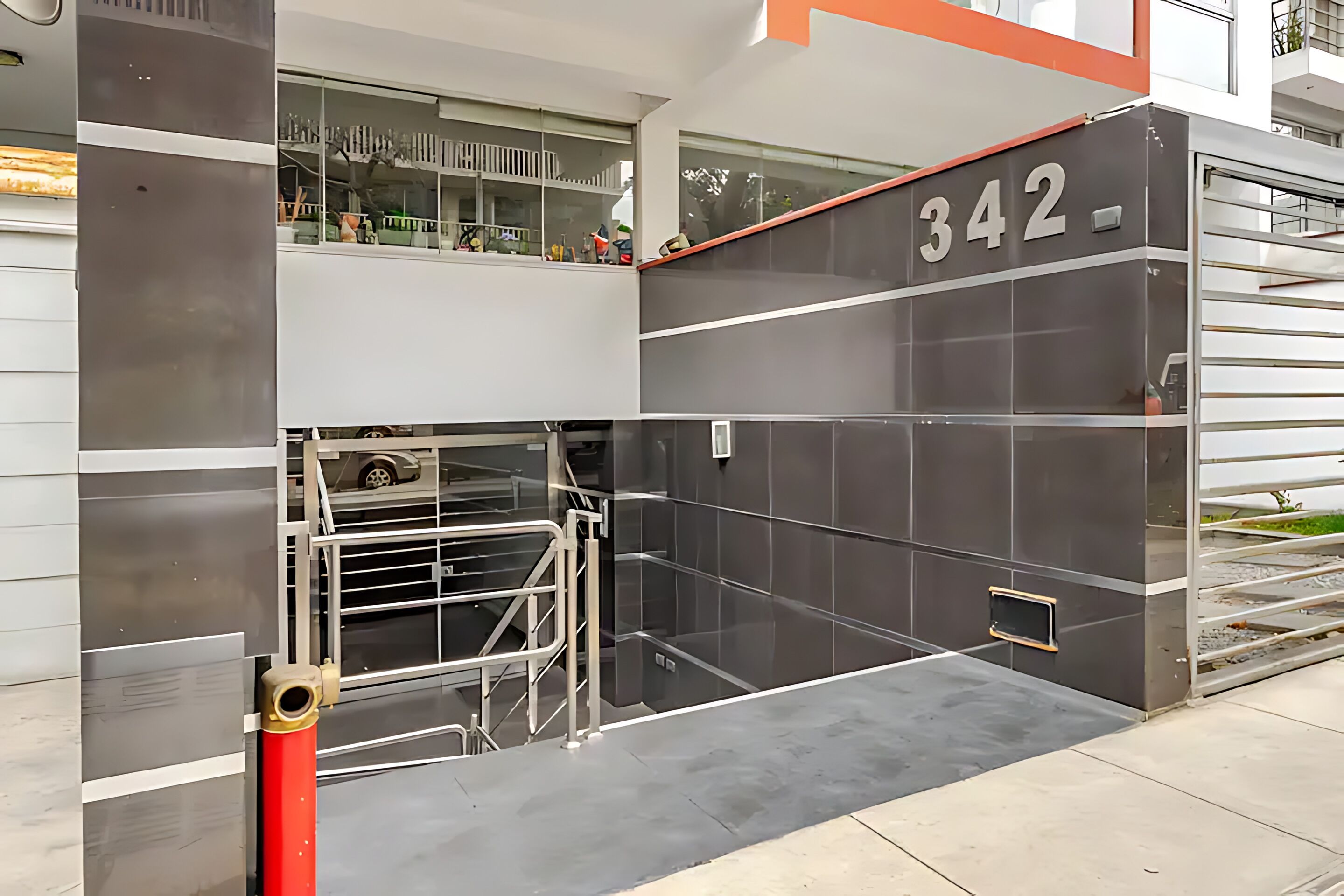Una entrada moderna de edificio con puerta de vidrio, portón de metal y el número '342' en la pared.