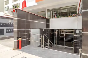 Ingresso di un edificio moderno con porta in vetro, cancello in metallo e un tubo antincendio rosso.