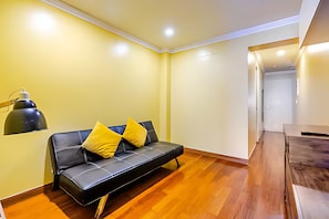 Un salon moderne avec un canapé en cuir noir, un parquet en bois et un lampadaire noir.