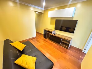 Una sala de estar con un sofá negro, cojines amarillos, un mueble de entretenimiento de madera y un televisor montado.