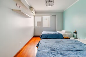 A bedroom with two beds, a window, a nightstand, and a lamp. - Stylish Miraflores Apt • Walk to Sea • WiFi • Optional AC • Parking (Miraflores)