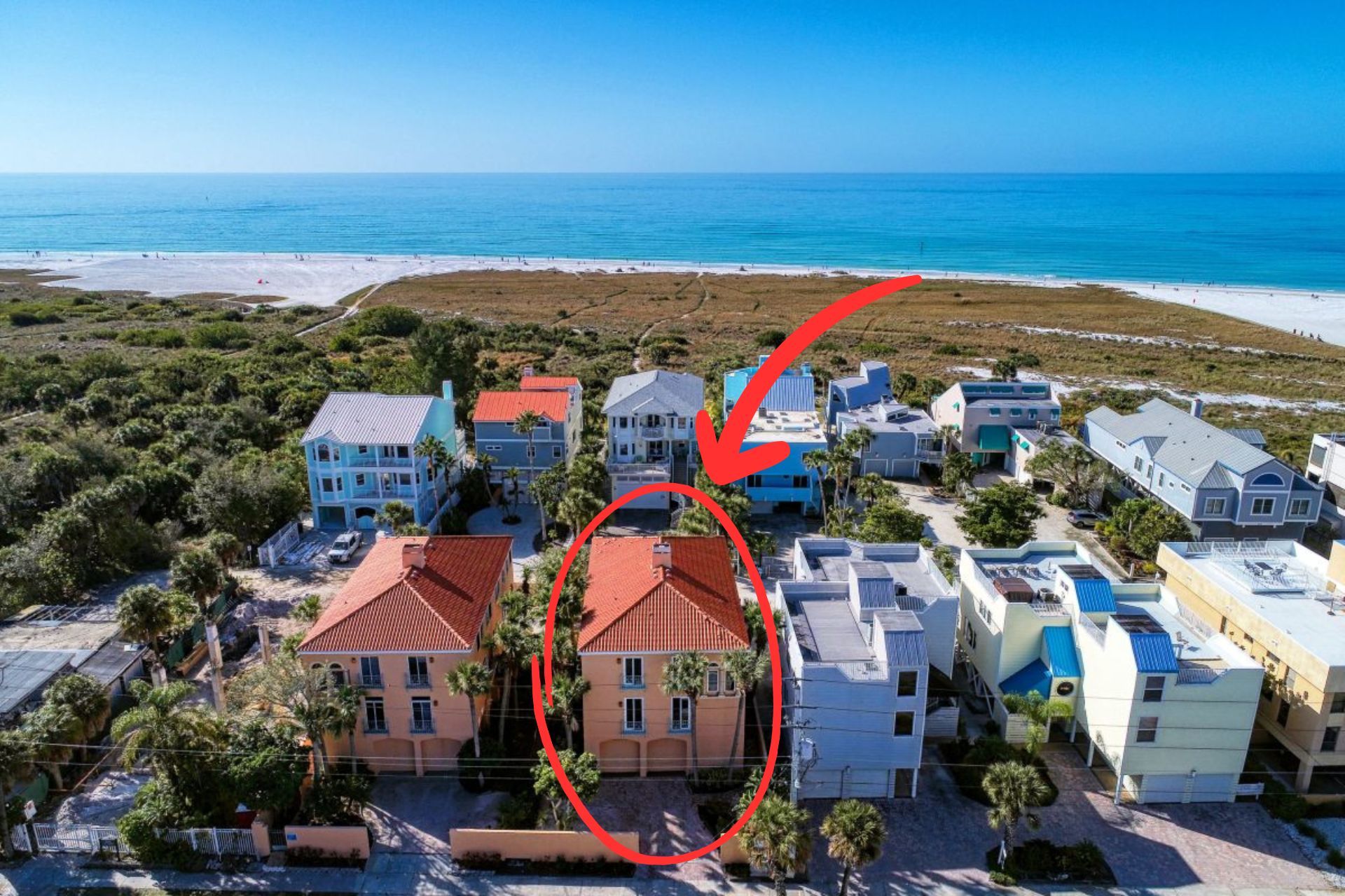 A coastal residential area with houses, some with red roofs, and a beach in the background.