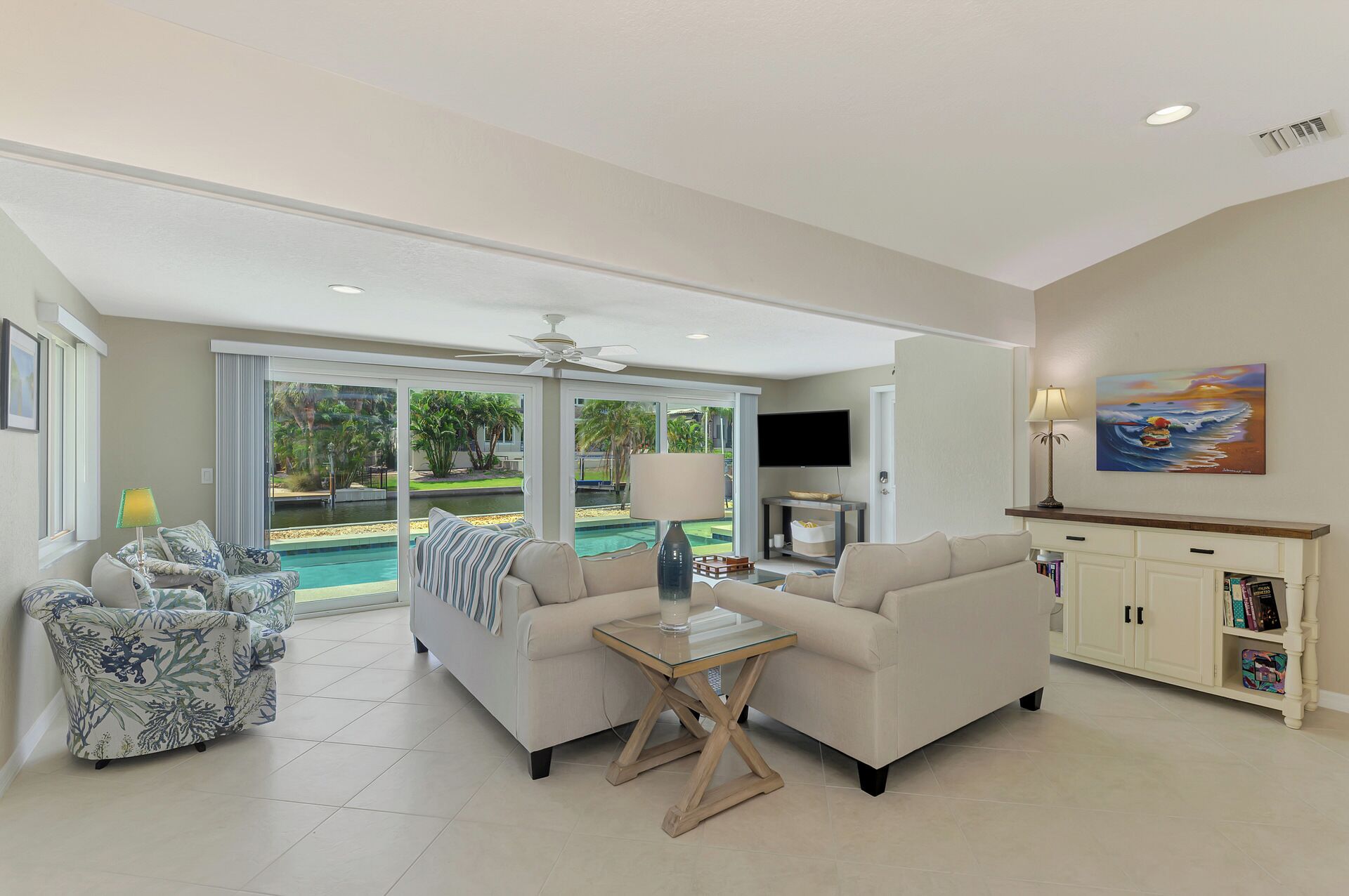 A spacious living room with a pool view, a flat-screen TV, and a bookshelf.