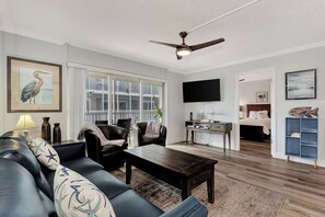 A living room with a dark wooden coffee table, a black leather sofa, and a ceiling fan.
