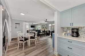 A modern kitchen with light blue cabinets, a dining area with white chairs, and a ceiling fan.