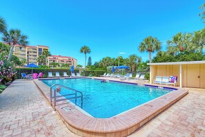 A swimming pool with a brick deck, lounge chairs, and umbrellas.