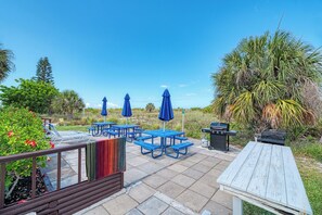 An outdoor patio with picnic tables, blue umbrellas, and a barbecue grill.