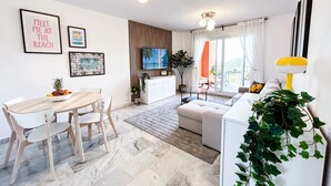 Ein modernes Wohnzimmer mit Essbereich, einer Couch, einem Fernseher und einer Pflanze.