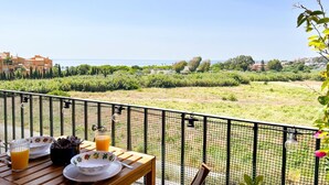 Ein Balkon mit gedecktem Tisch für das Frühstück, mit Blick auf eine Küstenlandschaft mit Gebäuden und Grünflächen.
