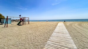 Ein Strand mit einer Holzstege, der zu einem Spielplatz mit einer Rutsche führt.