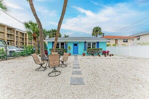 Een huis met een blauwe deur, een terras van grind en een zitgedeelte met stoelen en een tafel.