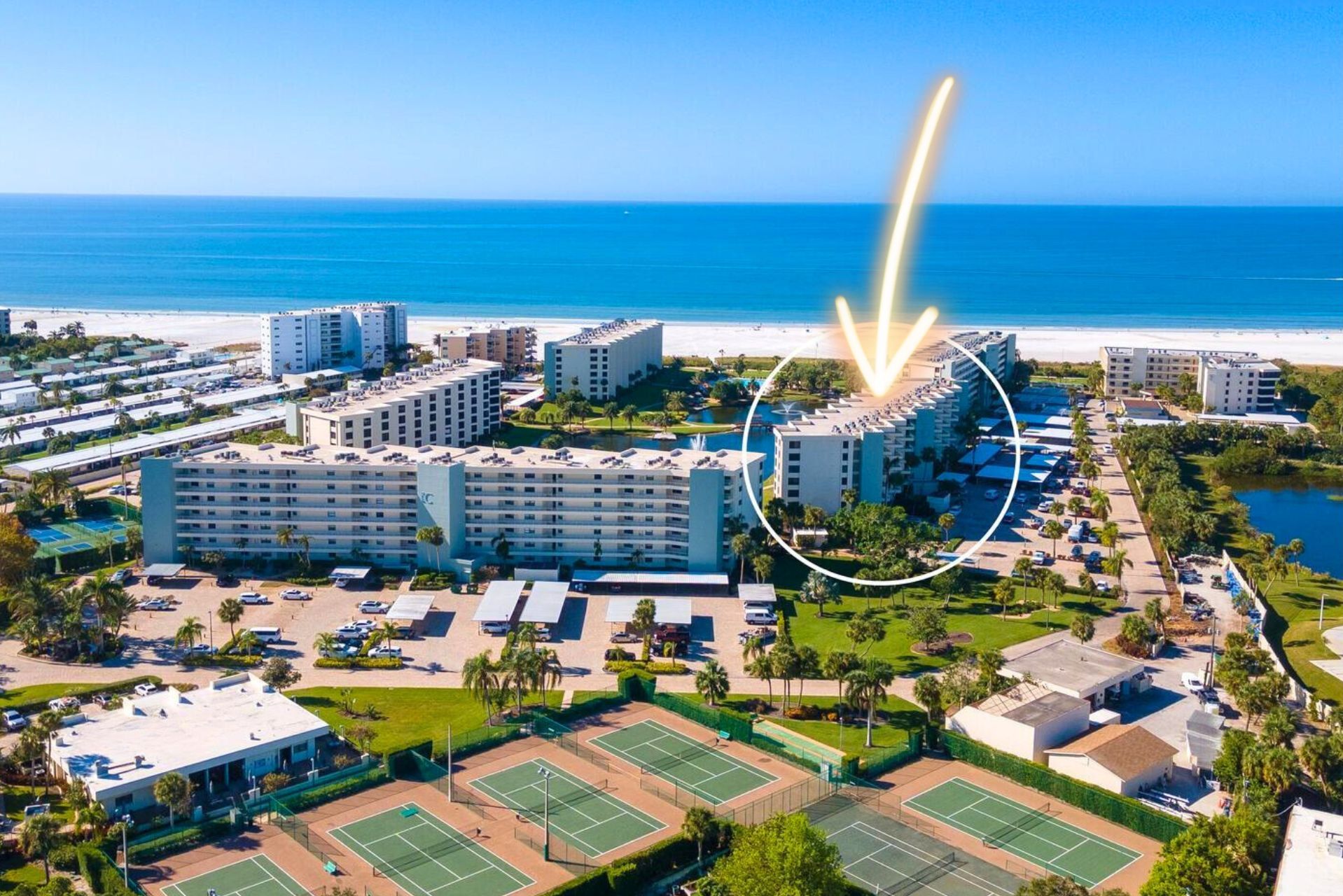 An aerial view of a coastal hotel complex with multiple buildings, a beach, and tennis courts.