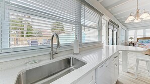 A modern kitchen with a stainless steel sink, white cabinetry, and a large window with blinds.