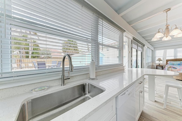 A modern kitchen with a stainless steel sink, white cabinetry, and a large window with blinds.