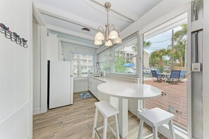Une cuisine dotée d’un plan de travail blanc, d’un réfrigérateur et d’une fenêtre donnant sur une terrasse aménagée avec du mobilier d’extérieur.