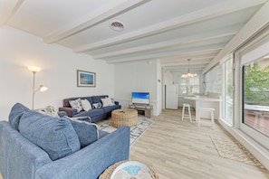 A modern living room with a blue sofa, a TV, and a dining area with a white table and chairs.