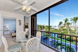 A balcony with a glass table and chairs, overlooking a parking area and palm trees.