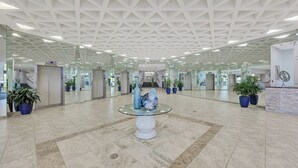 A spacious lobby with a geometric ceiling design, glass walls, and potted plants.