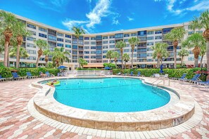 A hotel with a central swimming pool surrounded by lounge chairs and palm trees.