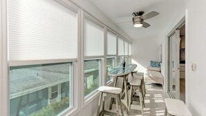 Ein helles Zimmer mit großen Fenstern, einem Deckenventilator und einem Glastisch mit Hocker.